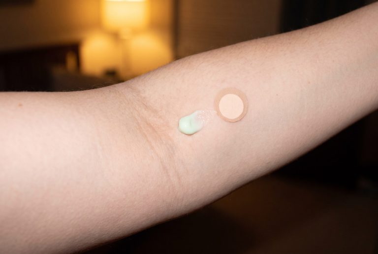 A small dab of pale green cream and a round bandage on the inner arm for a patch test