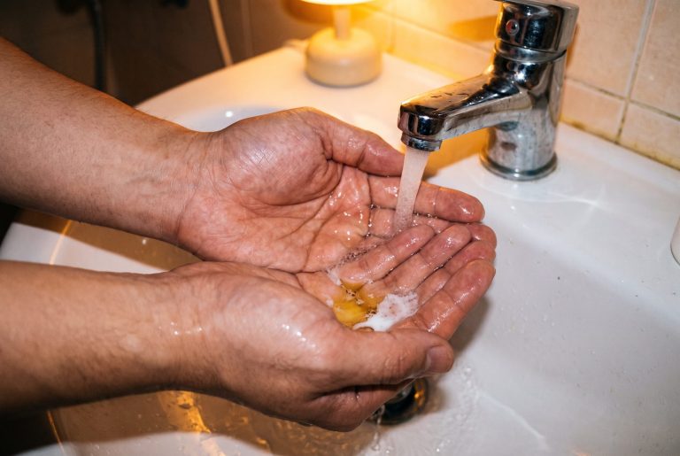 Cupped hands under a running tap as golden cleansing oil turns milky white in the water