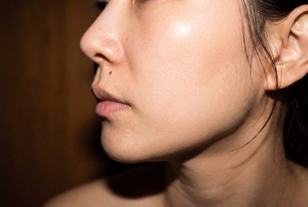 Profile of a woman's cheek and nose with a bright flash highlight on the cheekbone and visible pores