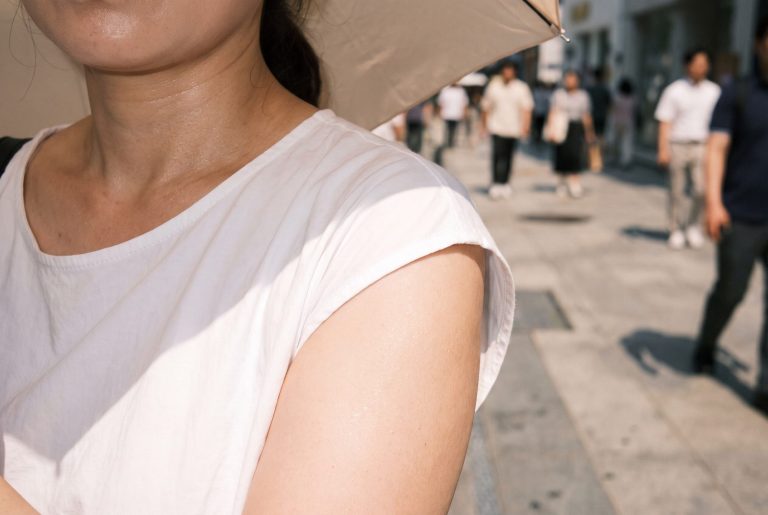 A woman shades herself with a parasol on a sunny Seoul street, its shadow edge across her shoulder