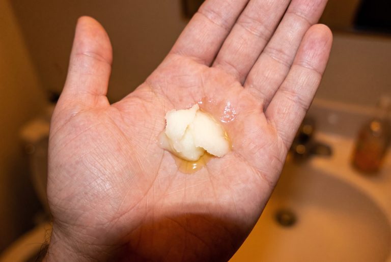 An open palm holds a dollop of cleansing balm that is melting into golden oil